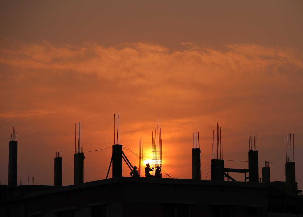 hero-img-02 Silhouette of workers on a construction site against a vibrant sunset sky.