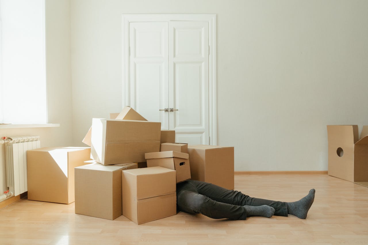 gallery-2 Person on floor surrounded by cardboard boxes during moving; concept of stress and relocation.
